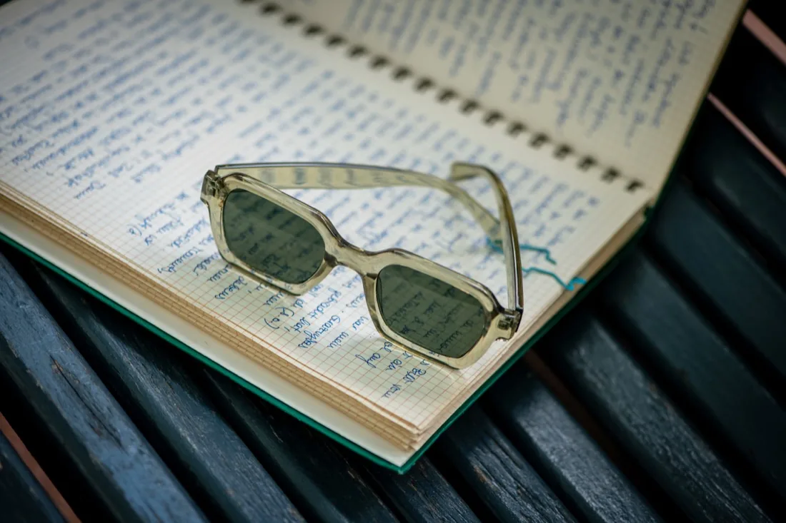 Aufgeschlagenes Notizbuch mit Sonnenbrille auf einer Holzbank