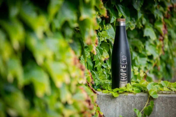 Schwarze Trinkflasche mit der Aufschrift Hope vor grünem Efeu