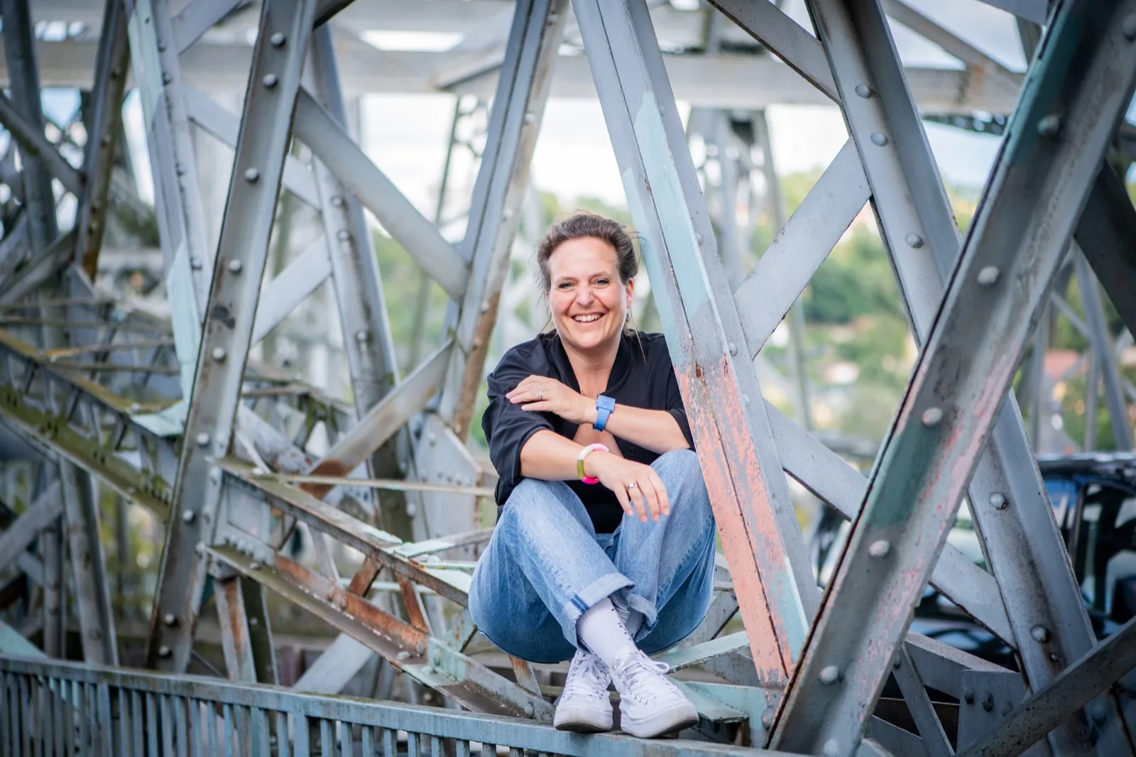 Annette Krönert sitzt lachend im Stahlgerüst einer Brücke – mehr Lebensfeste