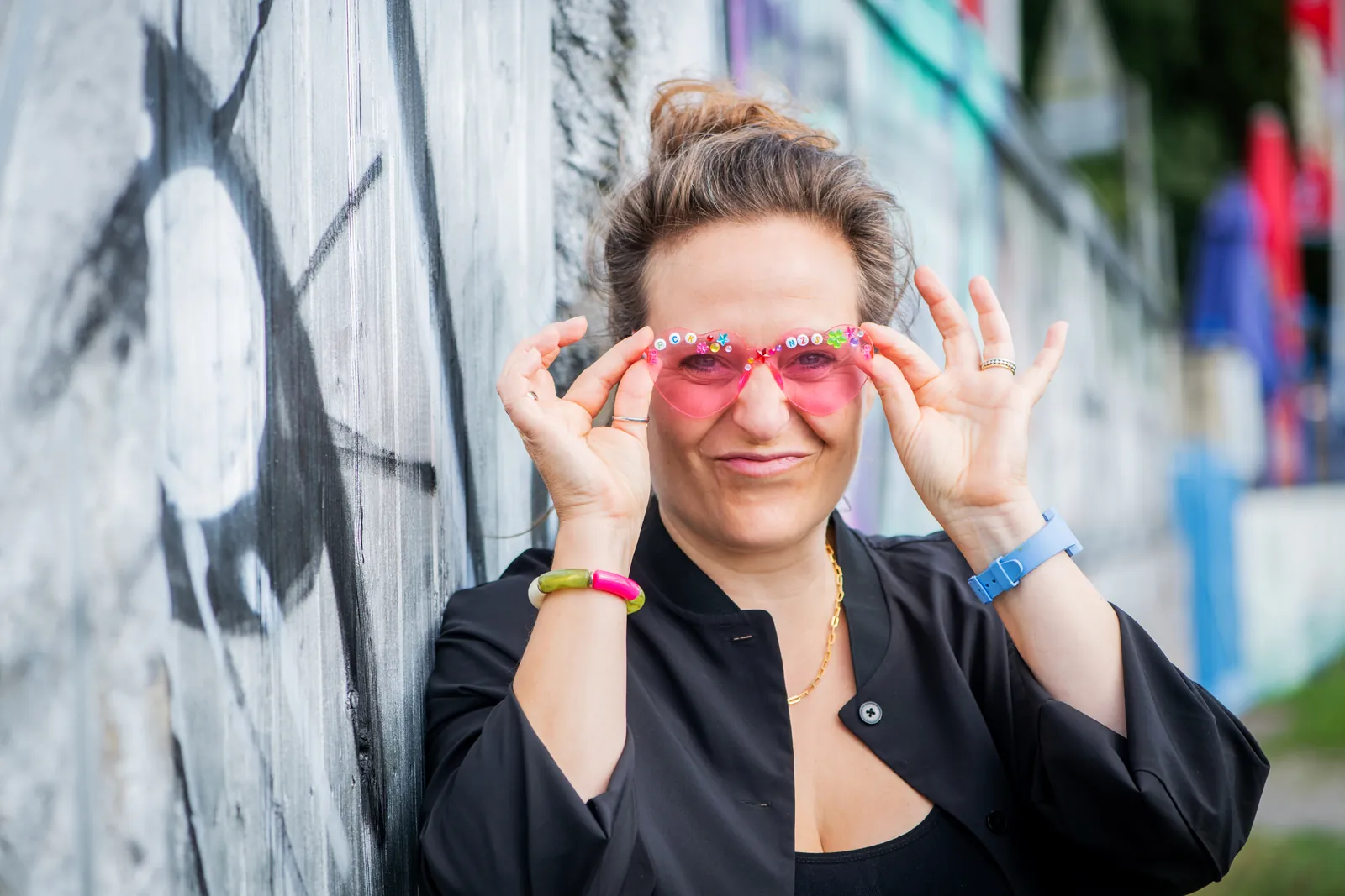 Freie Rednerin Annette Krönert mit rosa Herzbrille vor einer Graffiti-Wand