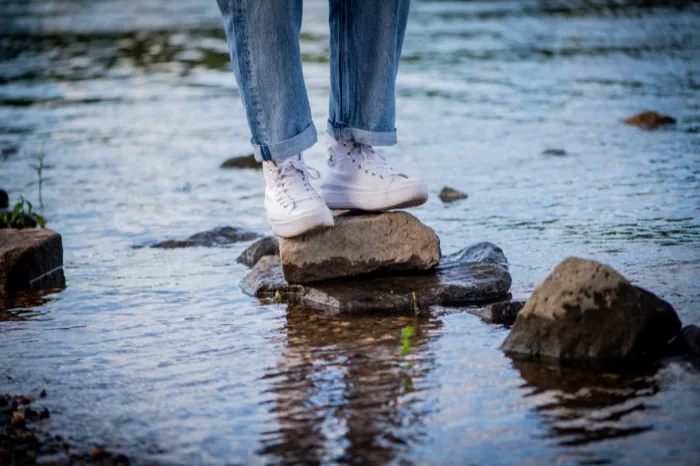Füße in weißen Sneakern auf einem Stein im flachen Flusswasser